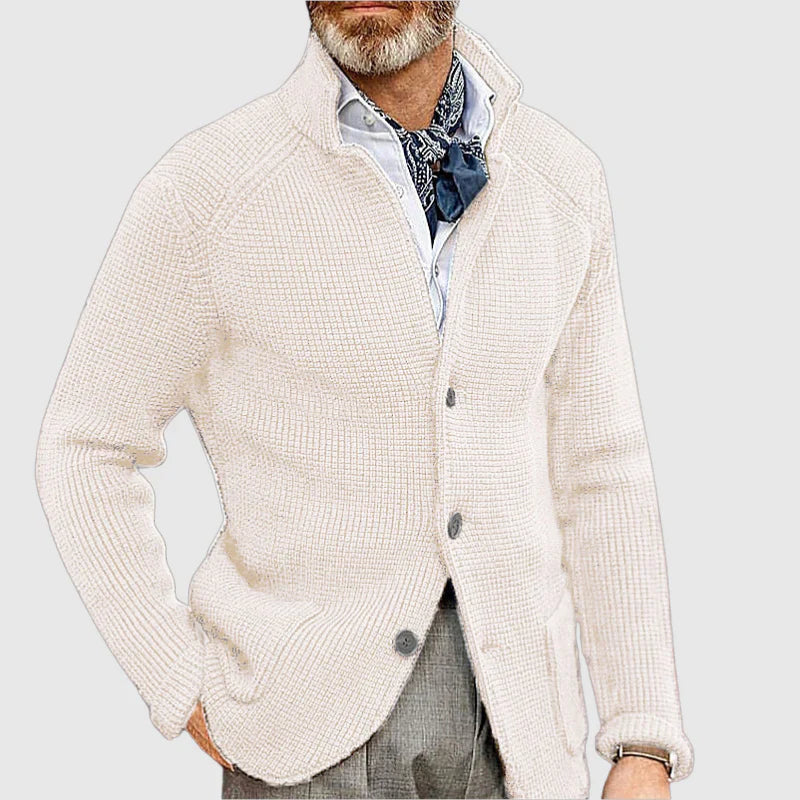 Man wearing a cream cardigan over a patterned shirt with a light gray background