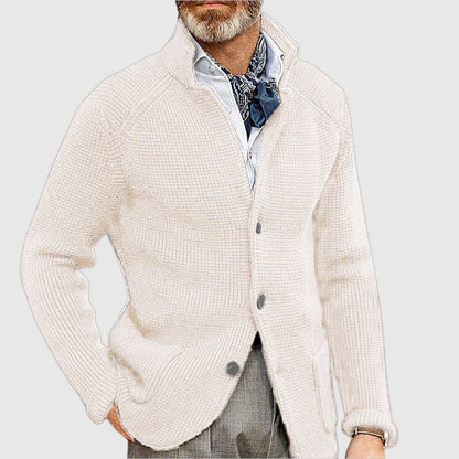 Man wearing a cream cardigan over a patterned shirt with a light gray background
