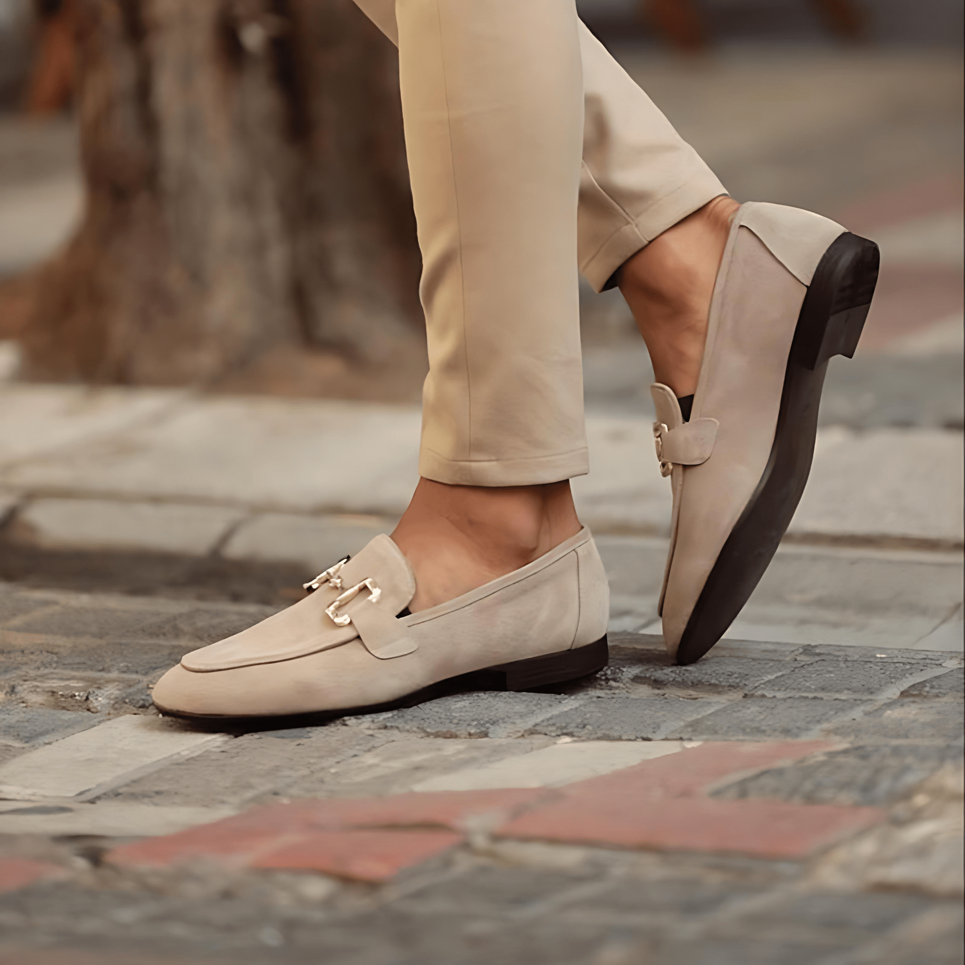 Beige loafers worn with beige pants on a stone pavement.
