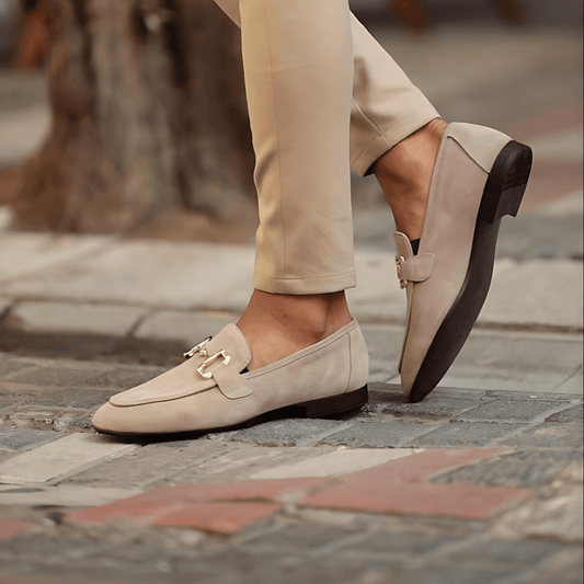 Beige loafers worn with beige pants on a stone pavement.