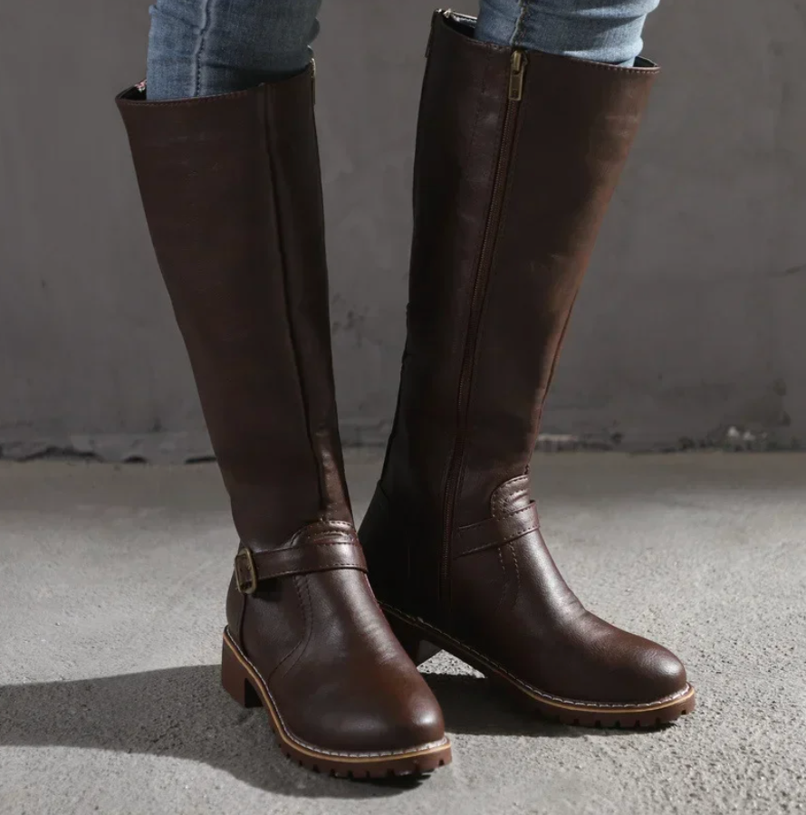 Brown knee-high boots worn with jeans against a neutral background
