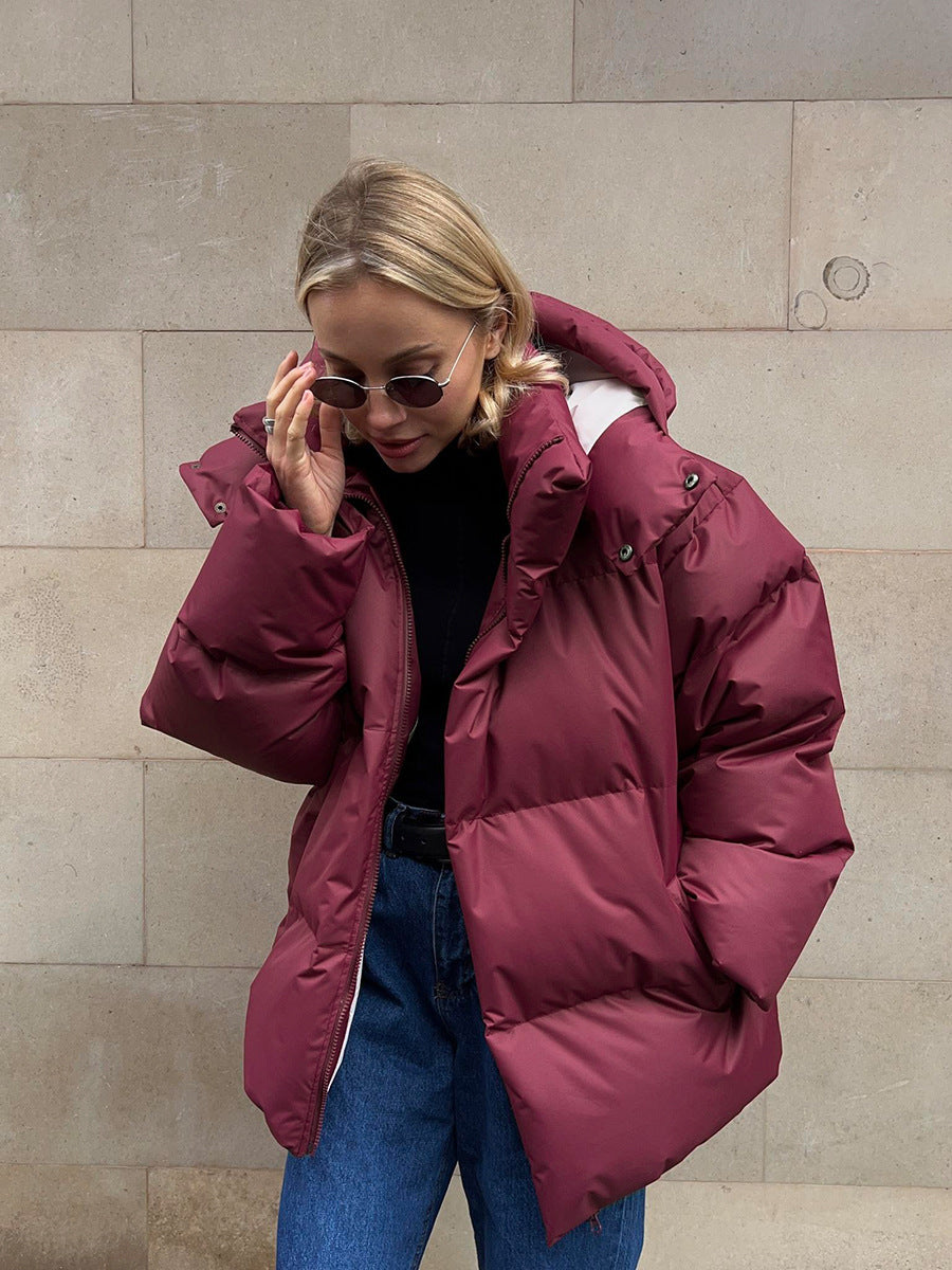 Woman wearing a burgundy puffer jacket against a beige wall.