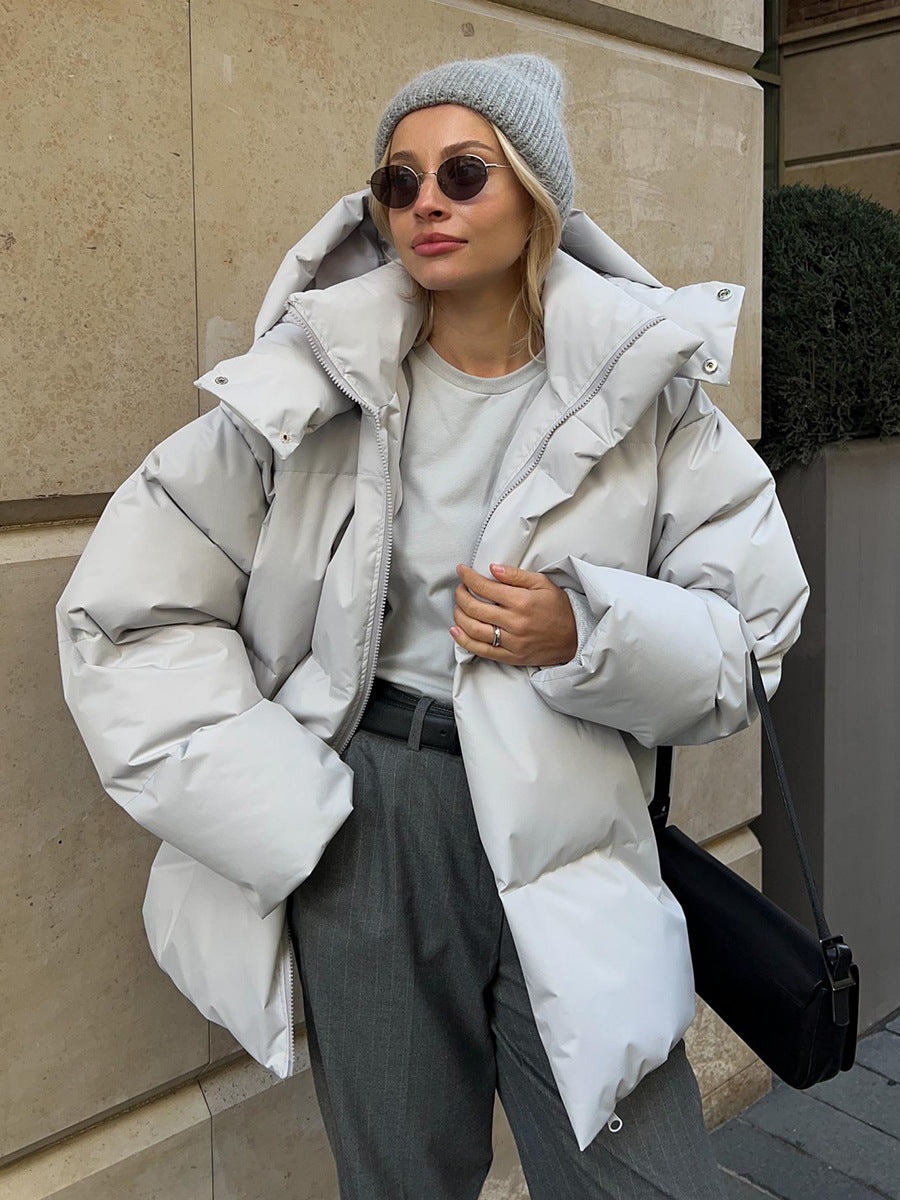 Person wearing a large white puffer jacket, gray beanie, and sunglasses outdoors.