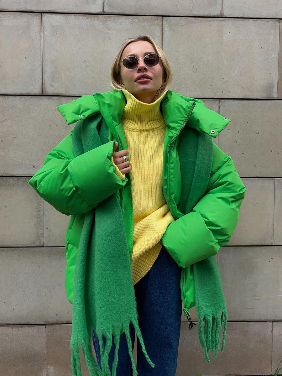 Person wearing a bright green coat with a yellow sweater and blue jeans against a stone wall.