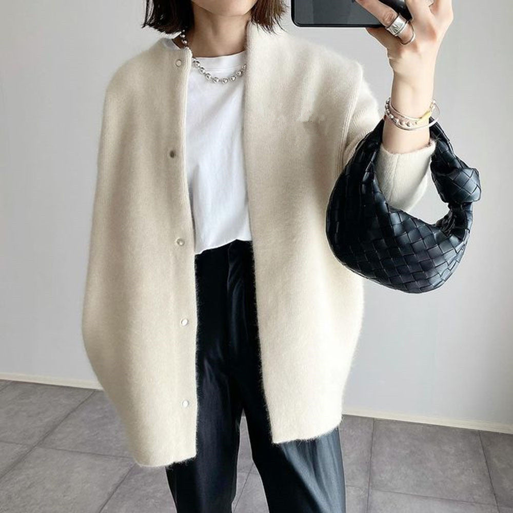 Person wearing a beige cardigan, white shirt, and black pants, holding a black handbag.