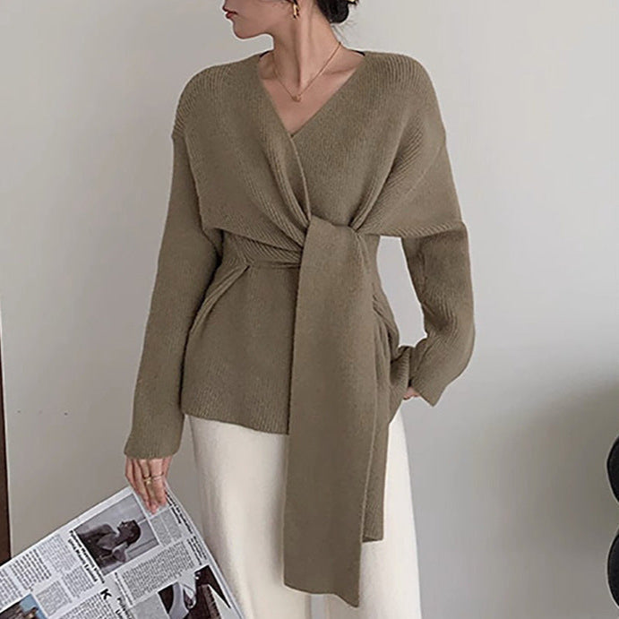 Woman wearing a brown knitted cardigan with a tie detail, holding a newspaper.