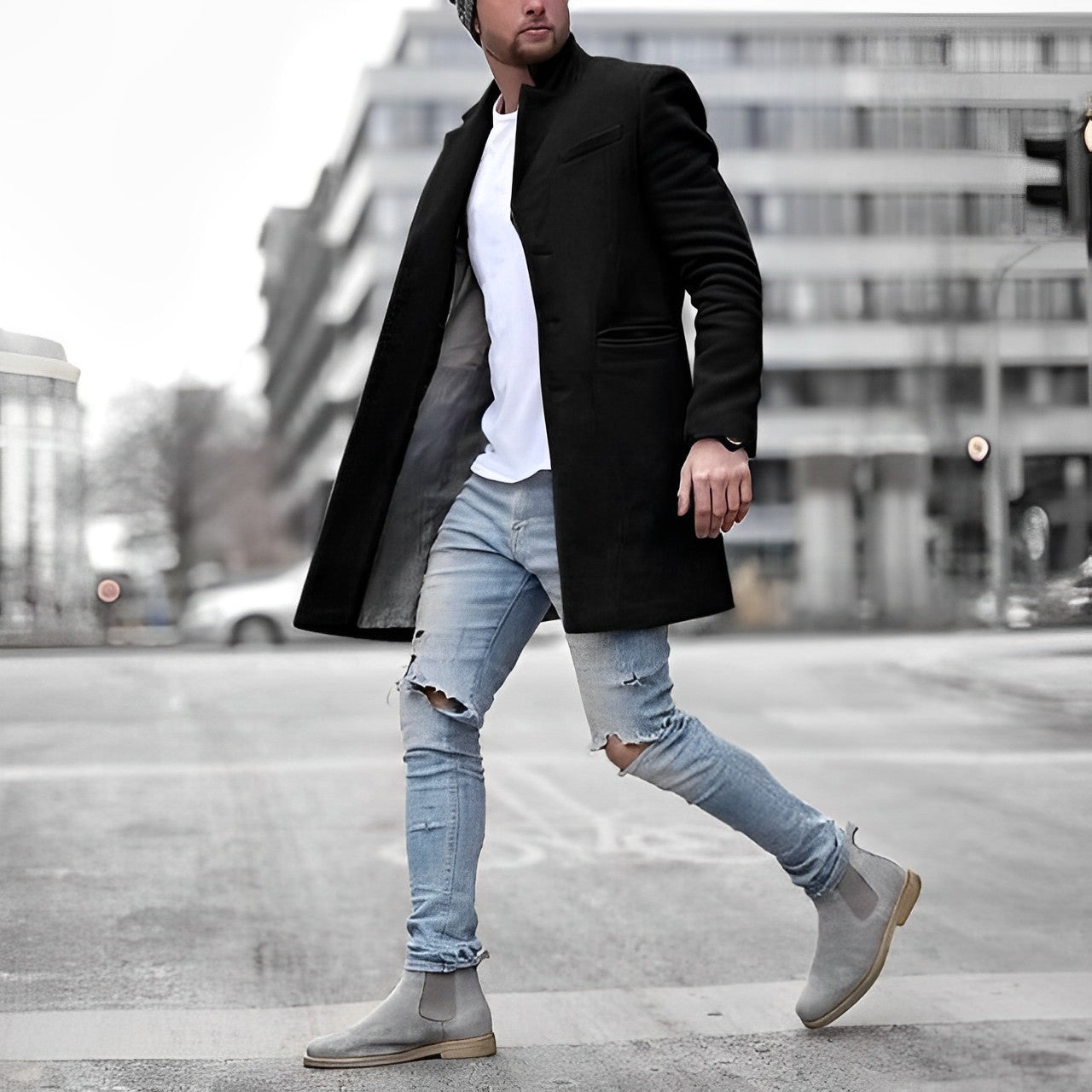Man wearing a black coat, white shirt, ripped jeans, and gray Chelsea boots on a city street.