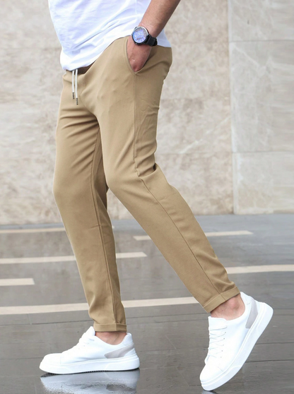 Person wearing beige pants and white sneakers against a neutral background