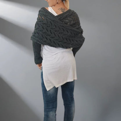 Person wearing a dark gray knitted shawl over a white top and blue jeans on a gray background