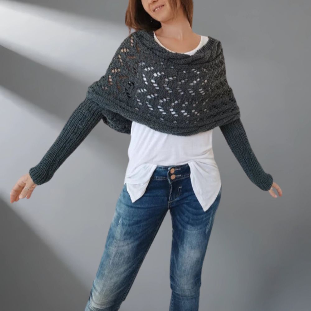 Person wearing a dark gray knitted shawl over a white shirt and blue jeans on a plain background