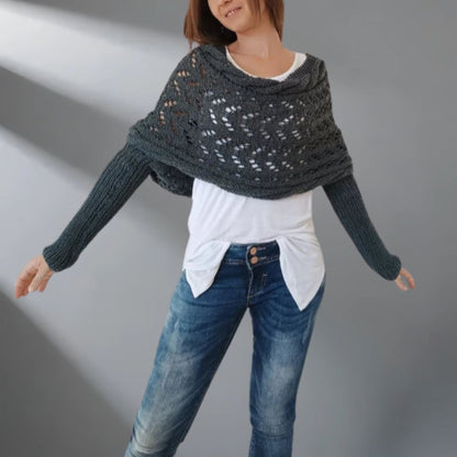 Person wearing a dark gray knitted shawl over a white shirt and blue jeans on a plain background