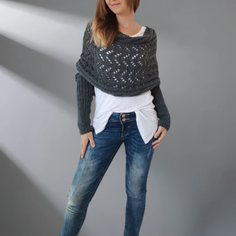 Person wearing a dark gray knitted shawl over a white shirt and blue jeans on a plain background