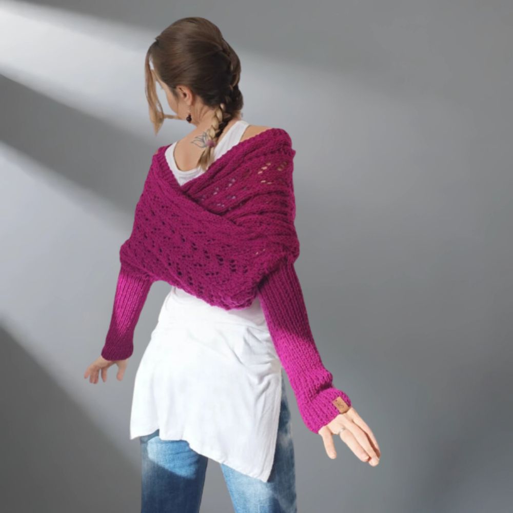 Woman wearing a purple knitted shawl over a white top and blue jeans on a gray background