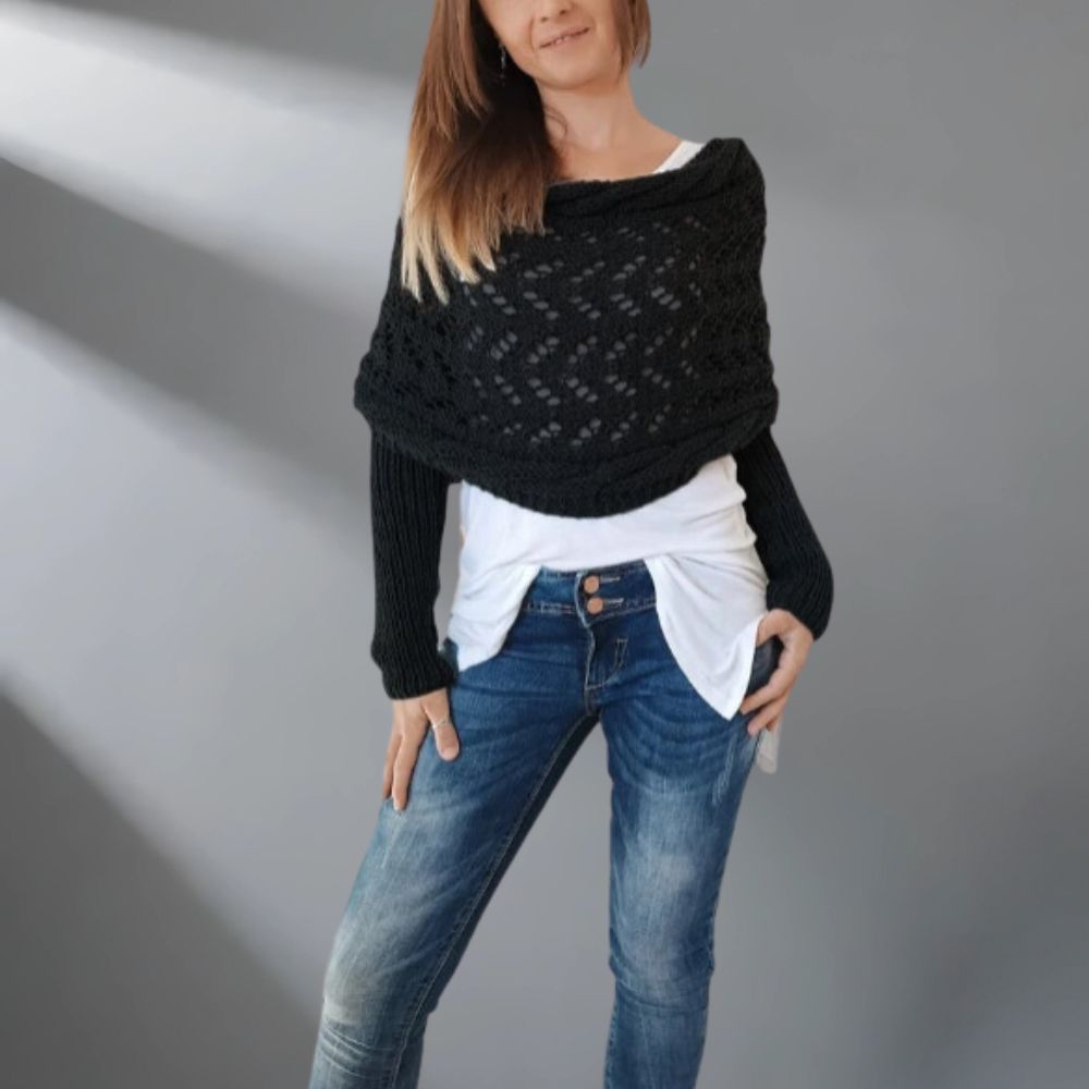 Woman wearing a black knitted shawl over a white top and blue jeans on a gray background