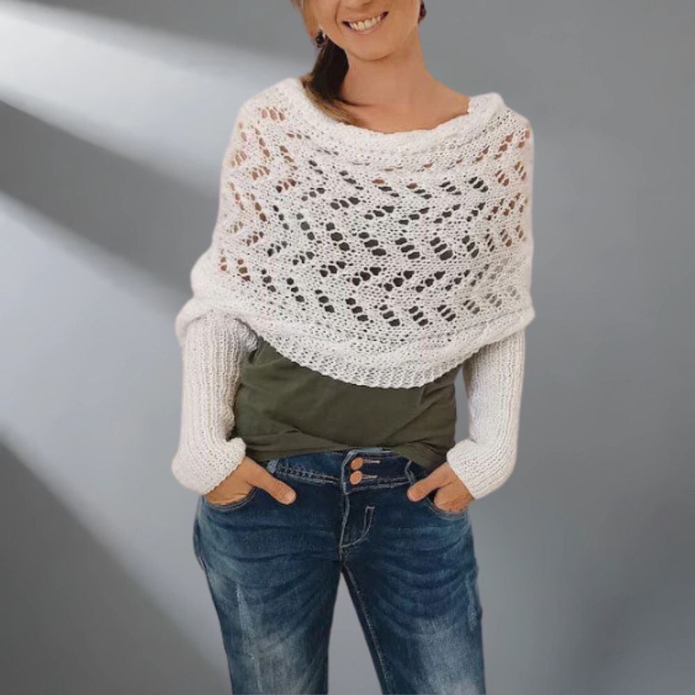 Woman wearing a white knitted shawl over a green top and blue jeans on a gray background
