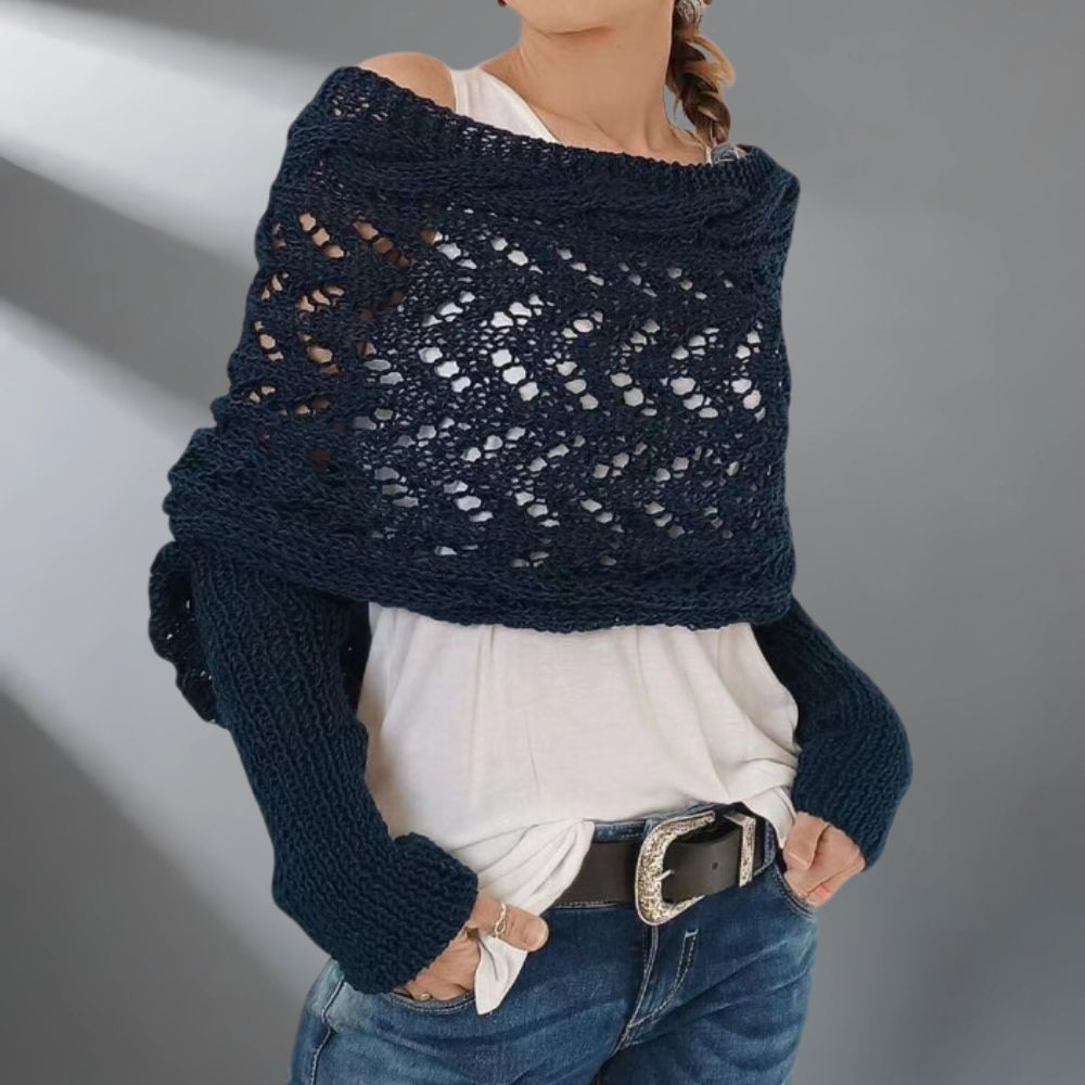 Person wearing a dark blue knitted shawl over a white top and jeans on a gray background