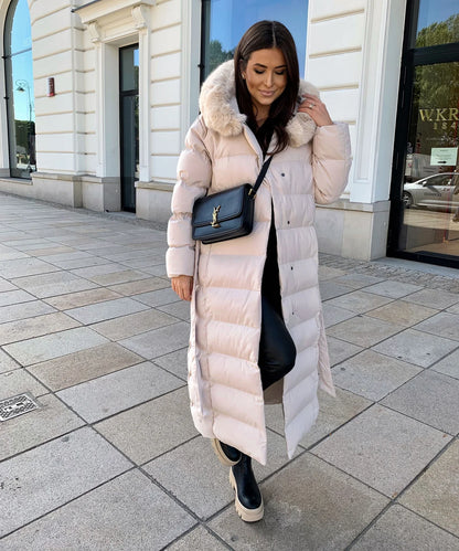 Woman wearing a long beige puffer coat with a fur hood on a city street.