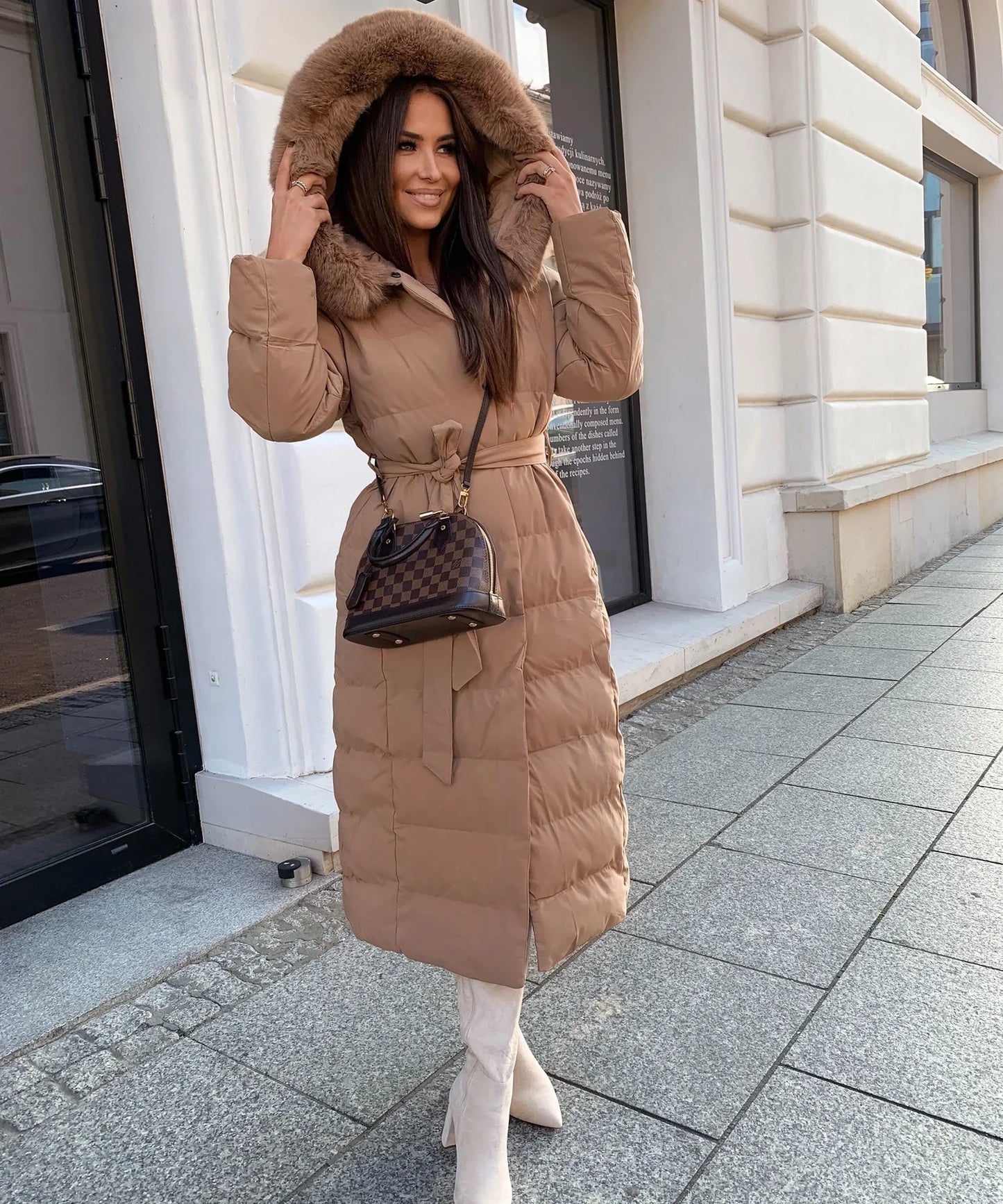 Woman wearing a long brown puffer coat on a city street.