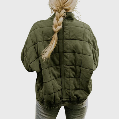 Person wearing a green quilted jacket with a plain background