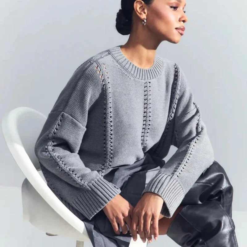 Woman wearing a gray sweater sitting on a white chair against a light gray background