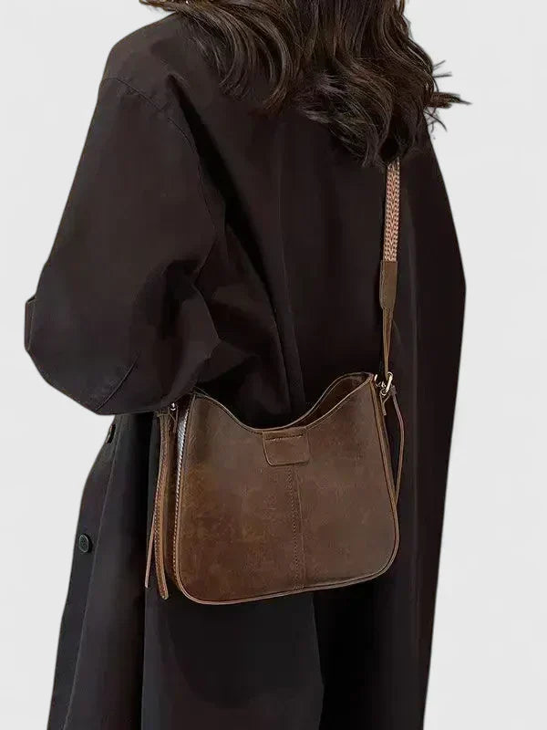 Person wearing a brown leather shoulder bag on a plain background
