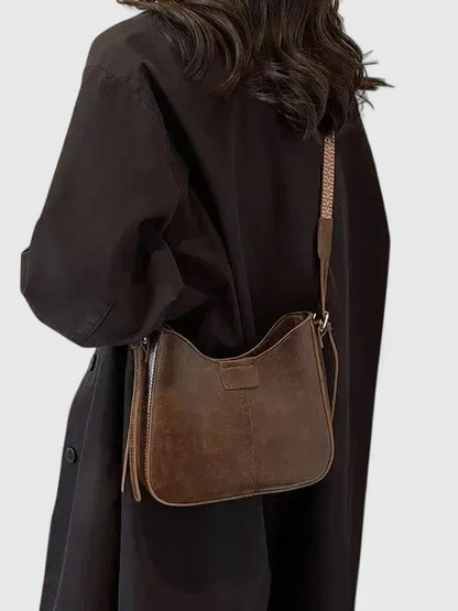 Person wearing a brown leather shoulder bag on a plain background