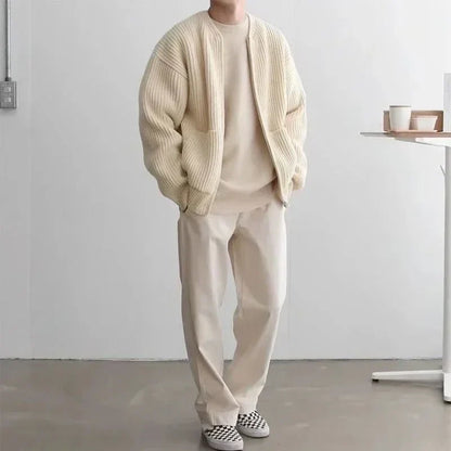 Person wearing a beige sweater and pants in a minimalistic room.