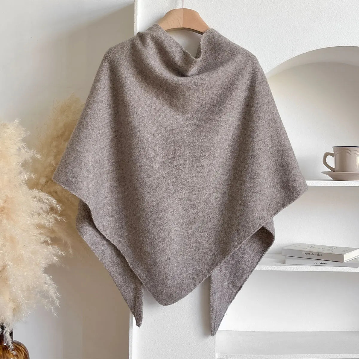 Gray poncho on a wooden hanger against a white wall with decor elements.