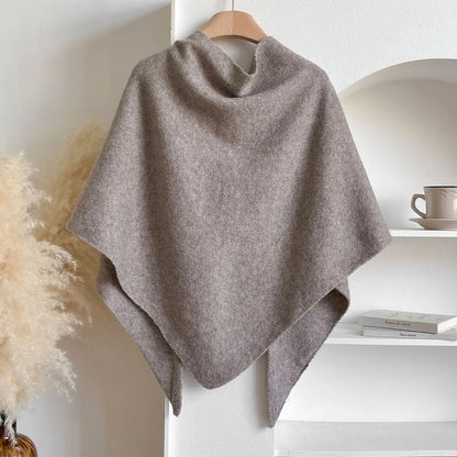 Gray poncho on a wooden hanger against a white wall with decor elements.
