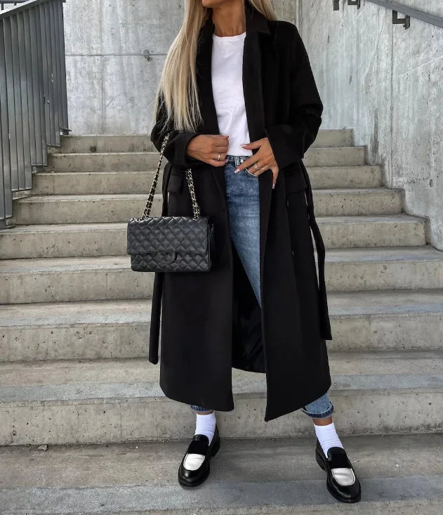 Person wearing a black coat and jeans, holding a black handbag on concrete steps.