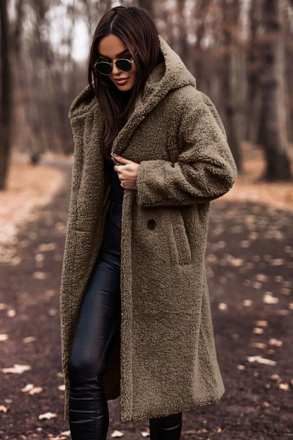 Woman wearing a long olive green coat in a forest setting