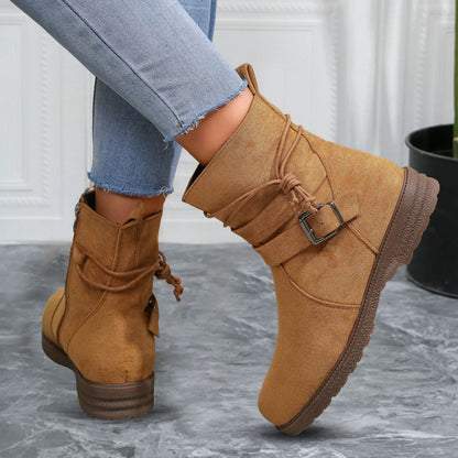 Tan suede boots with a buckle on a gray floor.