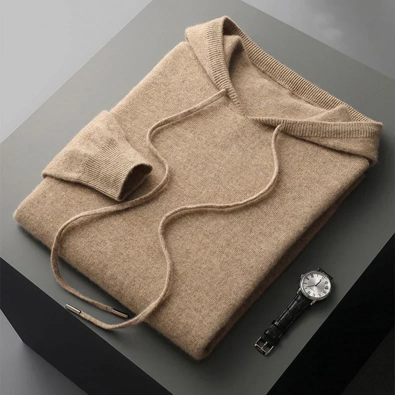 Folded beige sweater on a dark surface with a watch beside it