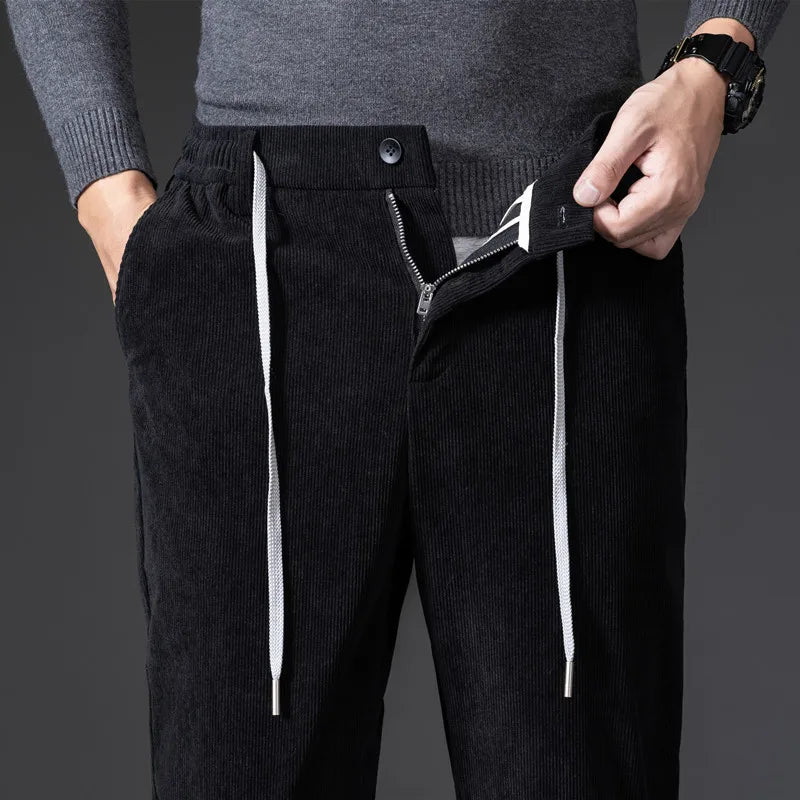 Person wearing black corduroy pants with white drawstrings on a dark background