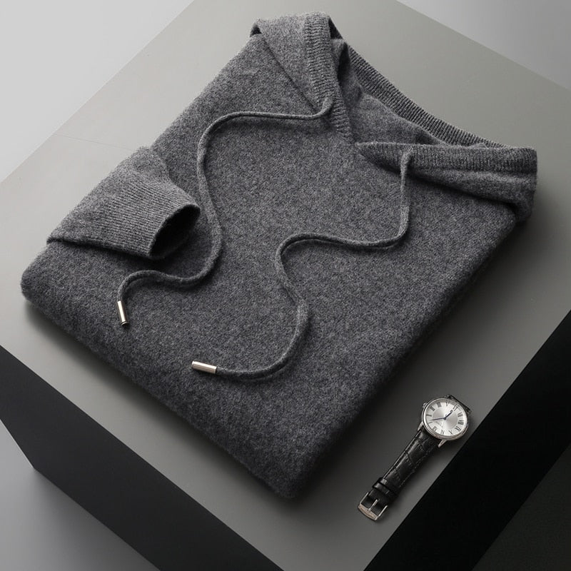 Folded gray sweater on a gray surface with a watch beside it