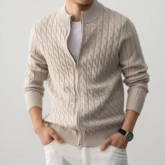 Man wearing a beige cable knit sweater over a white shirt on a gray background