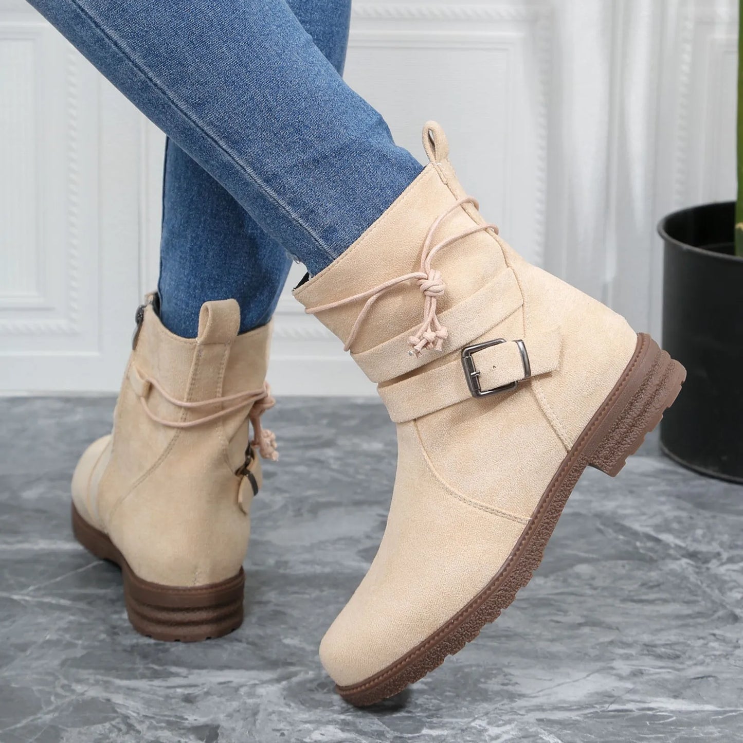Beige ankle boots with brown soles worn with blue jeans on a gray floor.