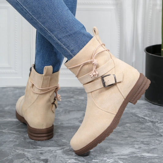 Beige ankle boots with brown soles worn with blue jeans on a gray floor.