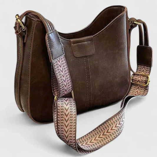 Brown leather handbag with a patterned strap on a light gray background