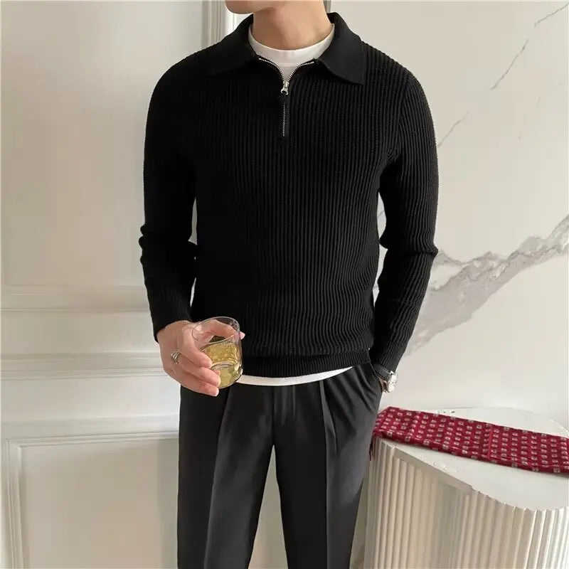 Person wearing a black ribbed sweater and dark pants holding a glass in an indoor setting.