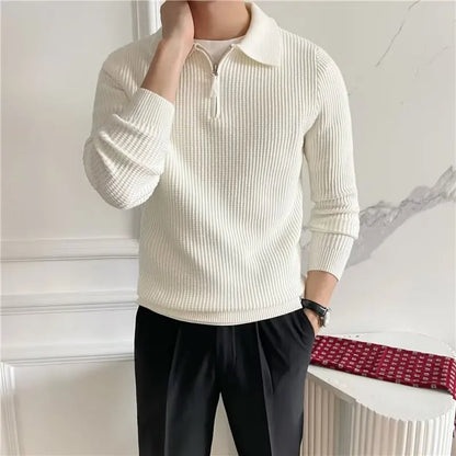 Person wearing a cream ribbed sweater and black pants with a white wall background