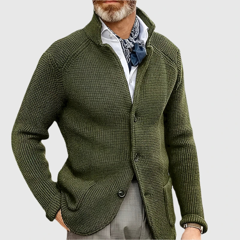 Man wearing a green knitted cardigan over a white shirt with a patterned scarf on a light gray background