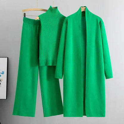 Green outfit with a coat, pants, and sweater on hangers against a gray background