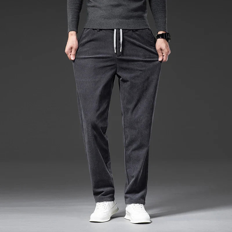 Person wearing dark gray jogger pants and a matching top on a gray background