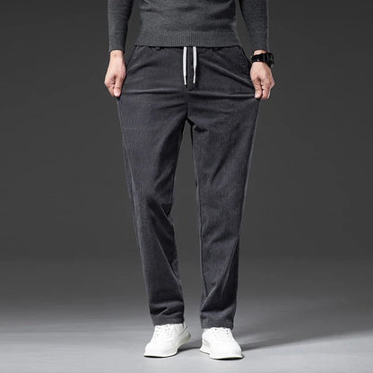 Person wearing dark gray jogger pants and a matching top on a gray background