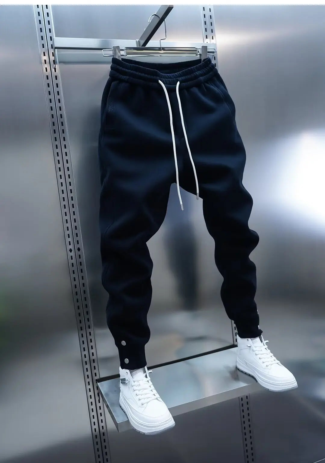 Black jogger pants with white drawstring and white sneakers on a metallic surface