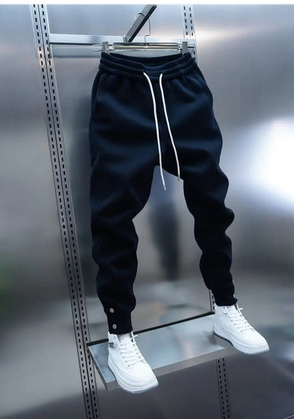 Black jogger pants with white drawstring and white sneakers on a metallic surface