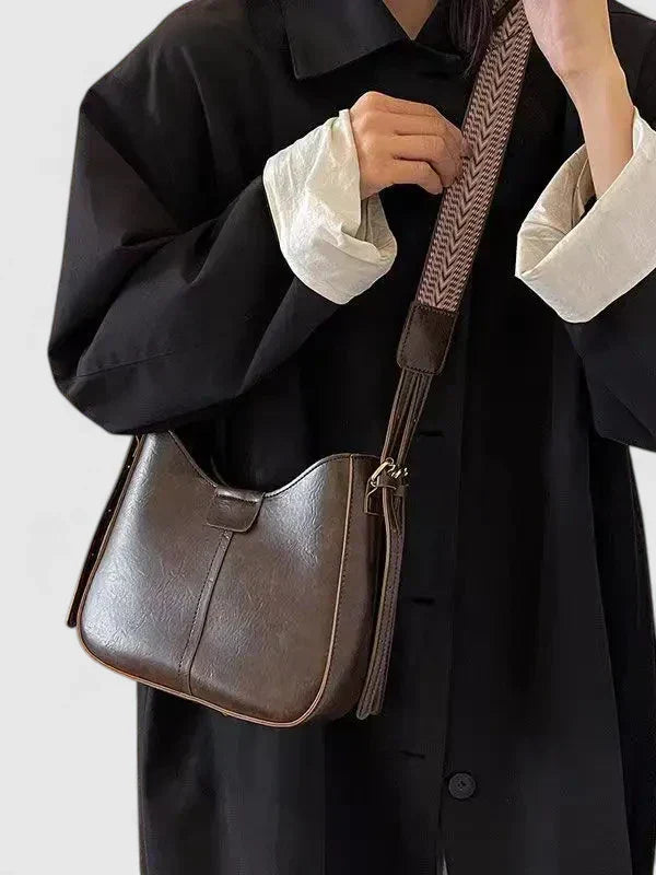 Person holding a brown leather handbag with a textured strap against a plain background