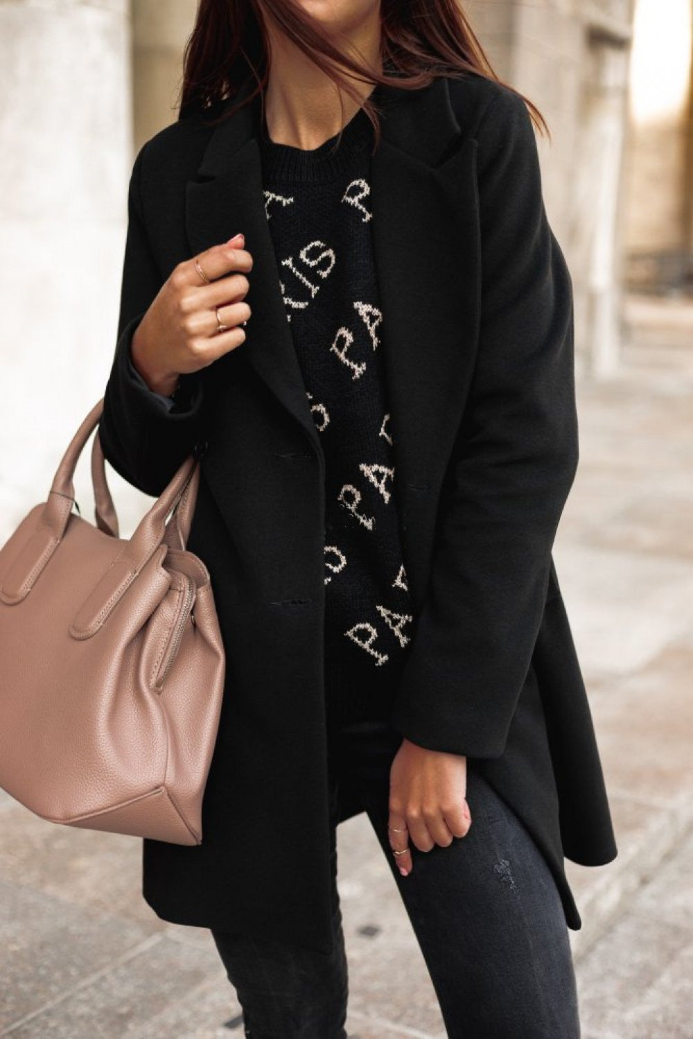 Person wearing a black coat and holding a pink handbag on a street.