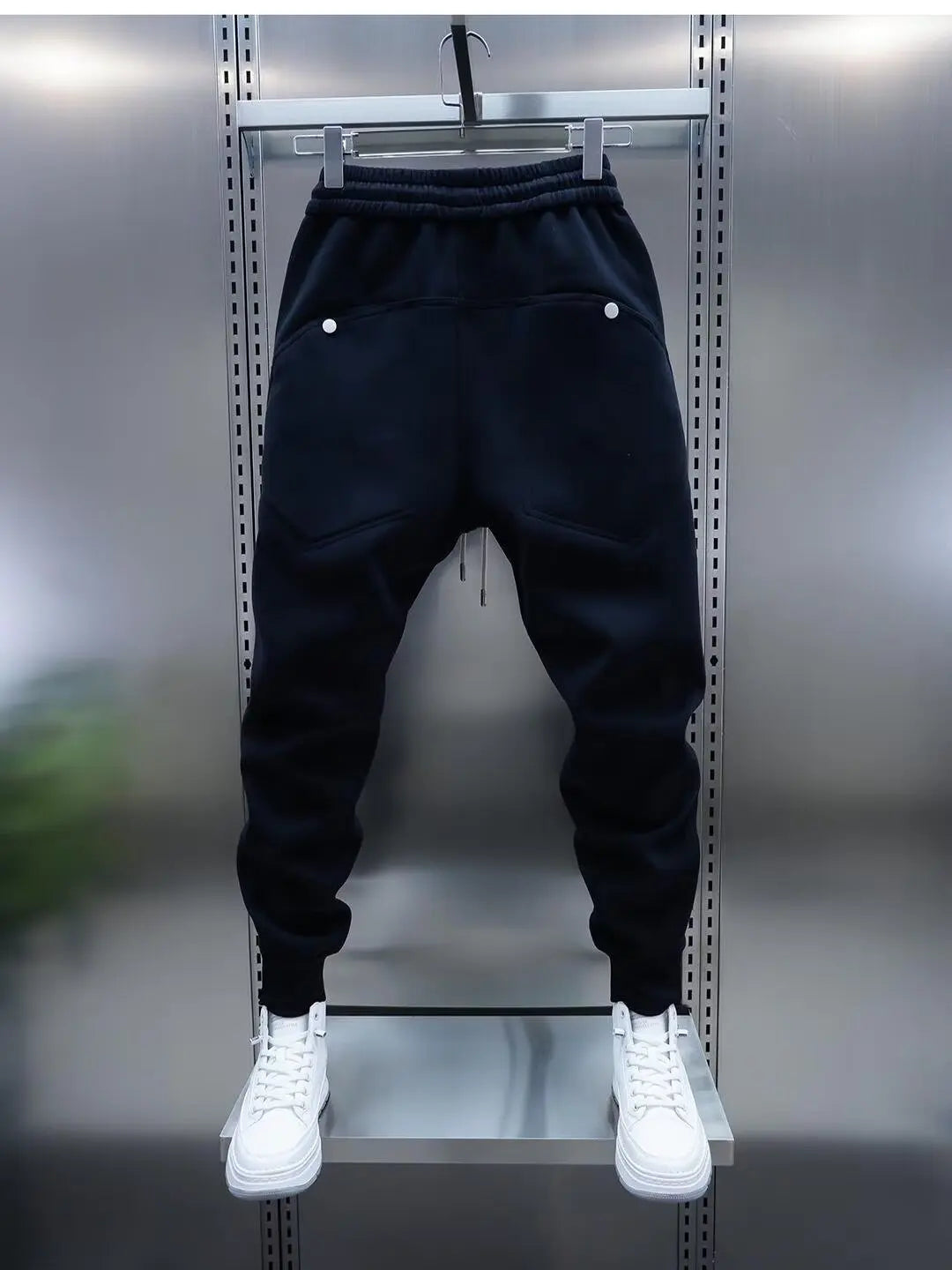 Black jogger pants on a hanger with white sneakers below against a metallic background